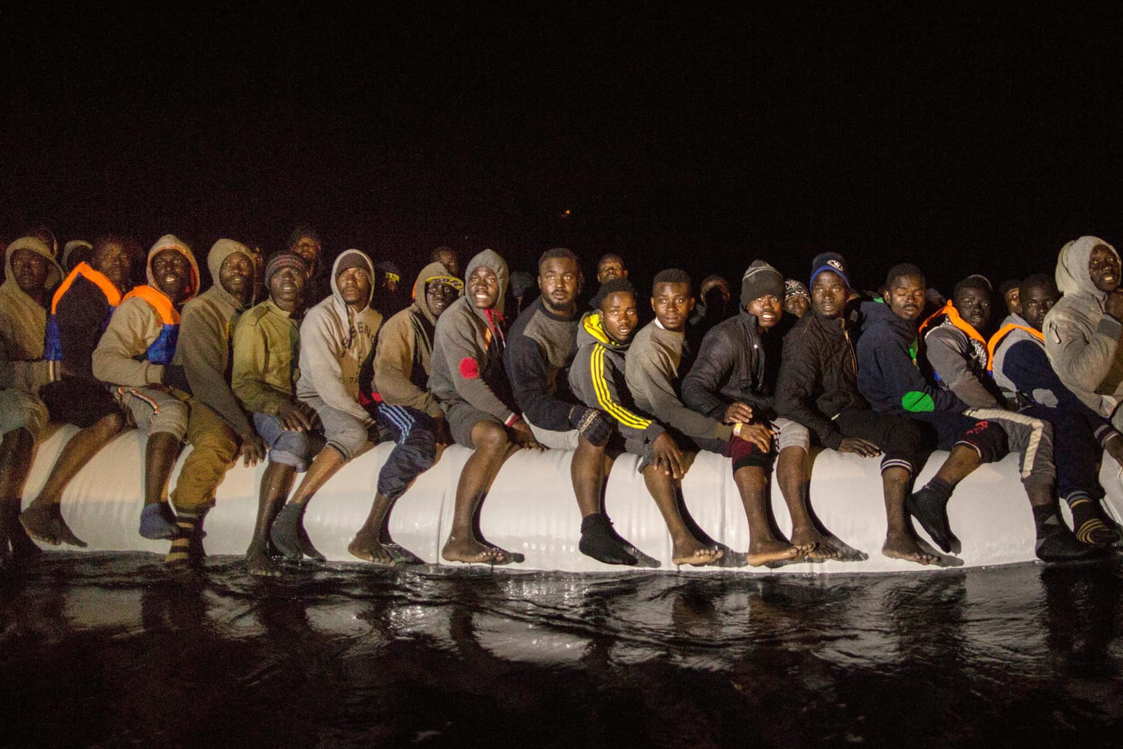 Flüchtlinge aus verschiedenen afrikanischen Staaten sitzen am frühen Morgen in einem überfüllten Schlauchboot auf dem Mittelmeer.