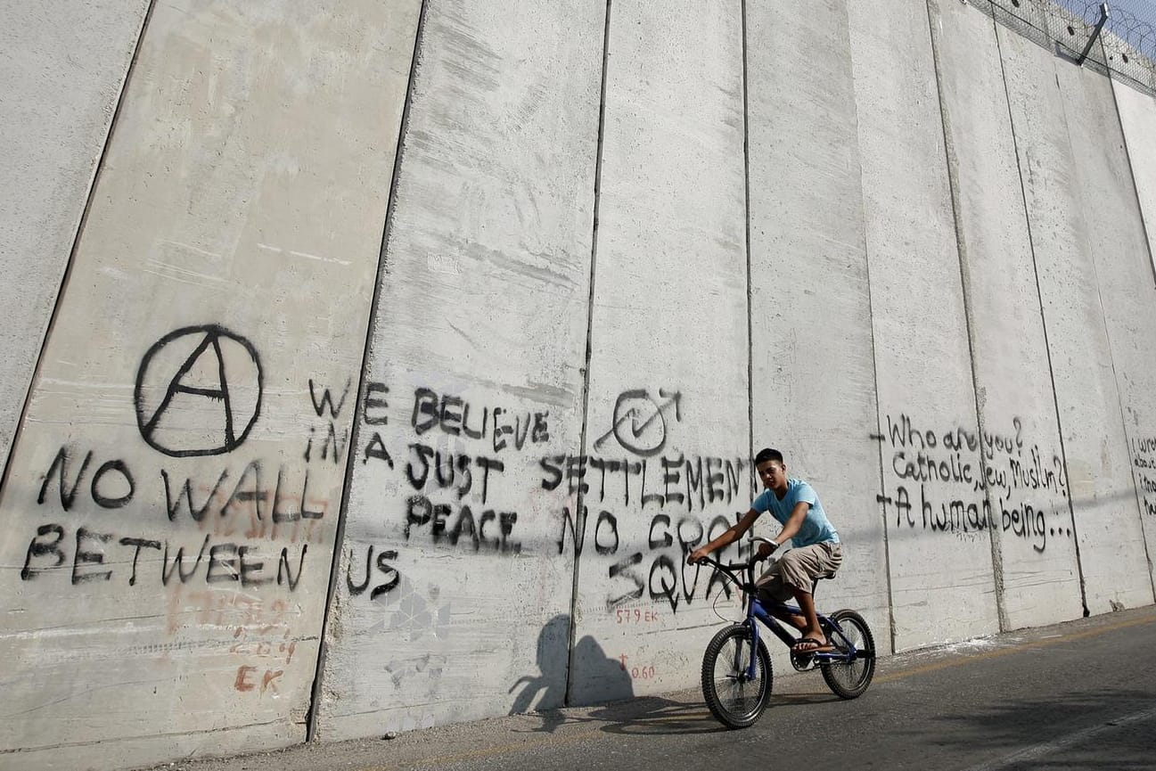 Ein arabischer Junge fährt mit einem Fahrrad an einer Mauer entlange, die Israel und Palästina in Ost-Jerusalem trennt.