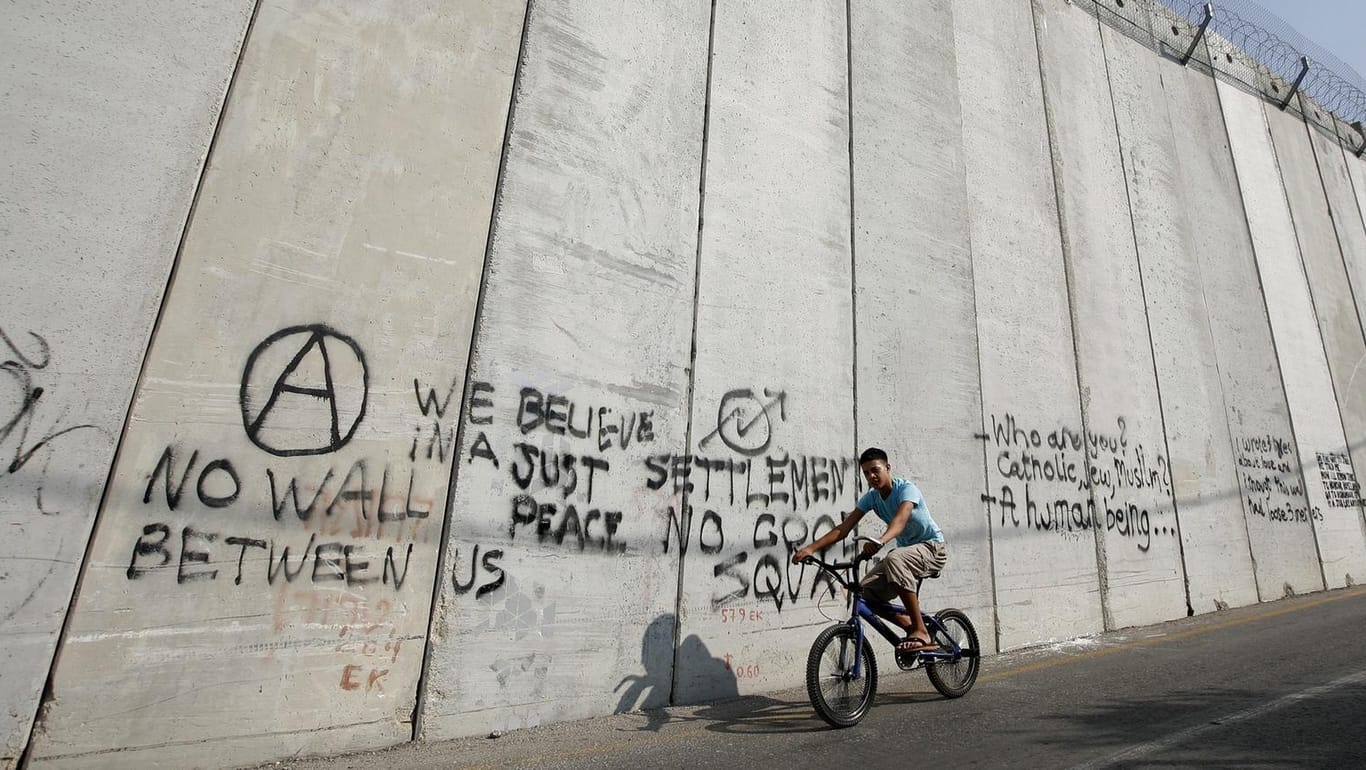 Ein arabischer Junge fährt mit einem Fahrrad an einer Mauer entlange, die Israel und Palästina in Ost-Jerusalem trennt.