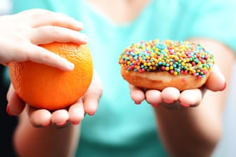 Eine Frau hält in der einen Hand eine Apfelsine, in der anderen einen Donut