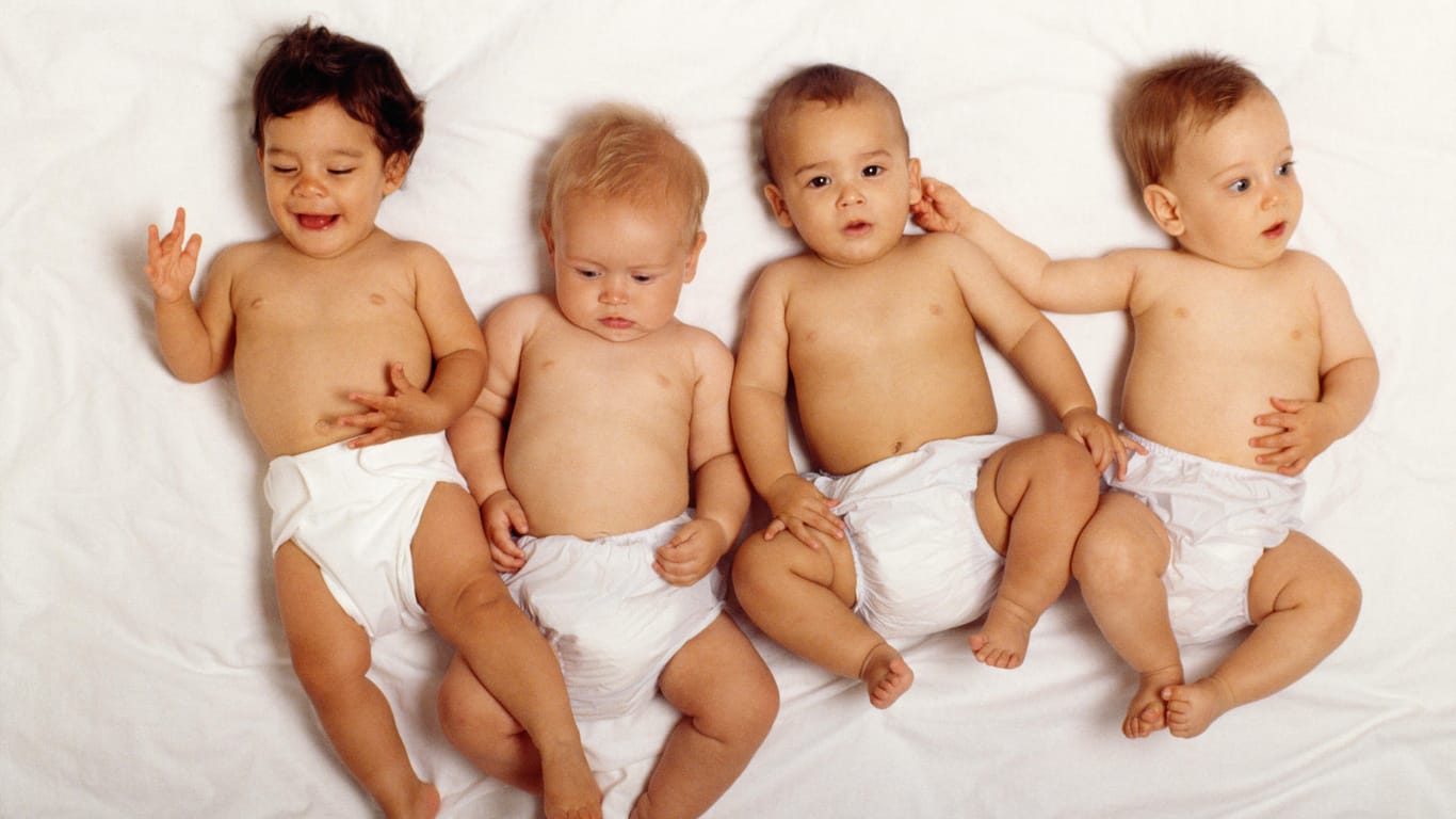 Vier Babys liegen nebeneinander auf einem weißen Bettlaken.