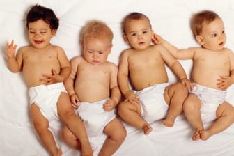 Vier Babys liegen nebeneinander auf einem weißen Bettlaken.