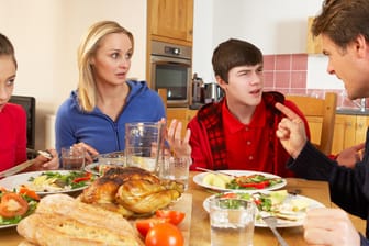 Eine Familie mit zwei jugendlichen Kindern streitet am Essentisch