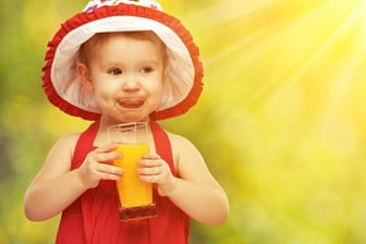 Ein kleines Mädchen trinkt ein Glas Orangensaft: Kinder trinken gerne Fruchtsäfte. Aber wie viele Gläser täglich sind in Ordnung?