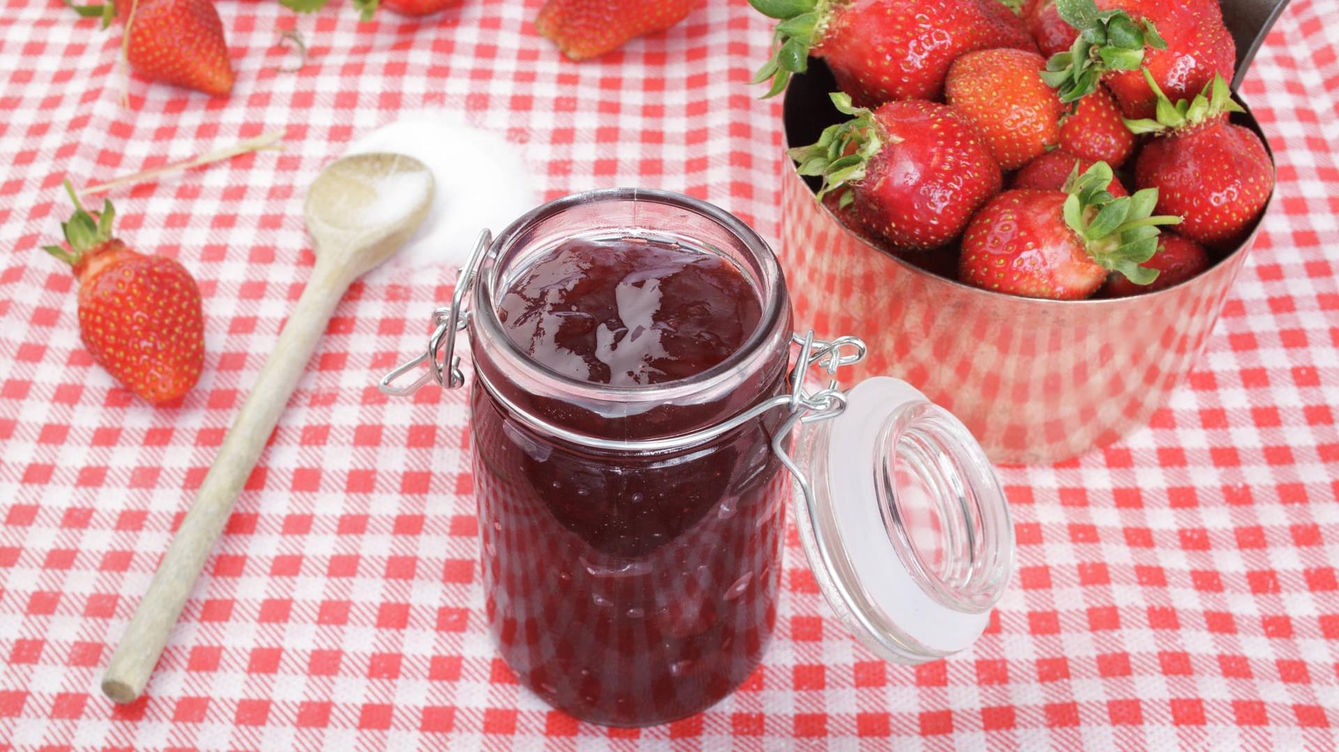 Erdbeeren im Kupferkessel und Zucker auf Holzlöffel