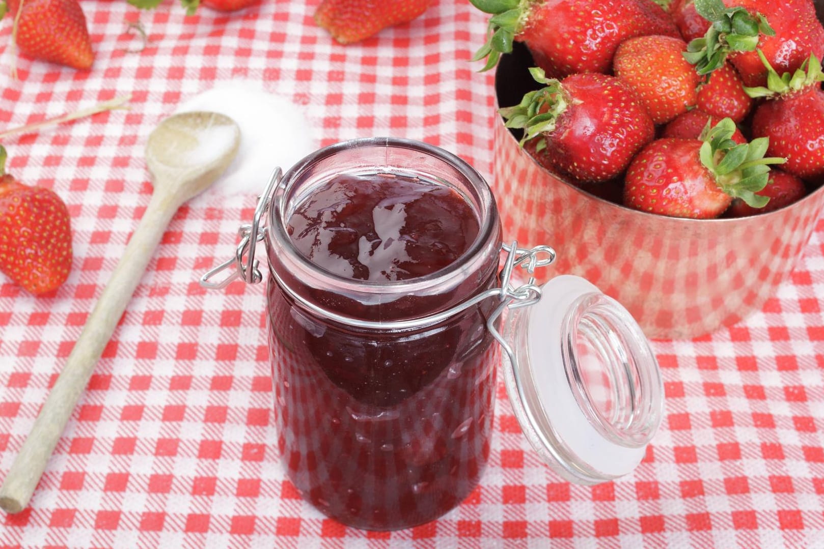 Erdbeeren im Kupferkessel und Zucker auf Holzlöffel