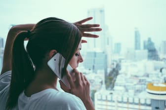 Frau telefoniert in Großstadt und schaut aus dem Fenster