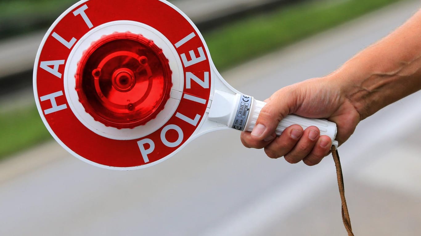 Ein Polizist hält eine Polizeikelle in der Hand mit der Aufschrift Halt Polizei Symbolbild Polizeikontrolle