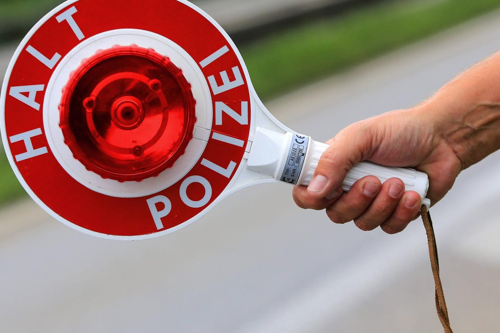 Ein Polizist hält eine Polizeikelle in der Hand mit der Aufschrift Halt Polizei Symbolbild Polizeikontrolle