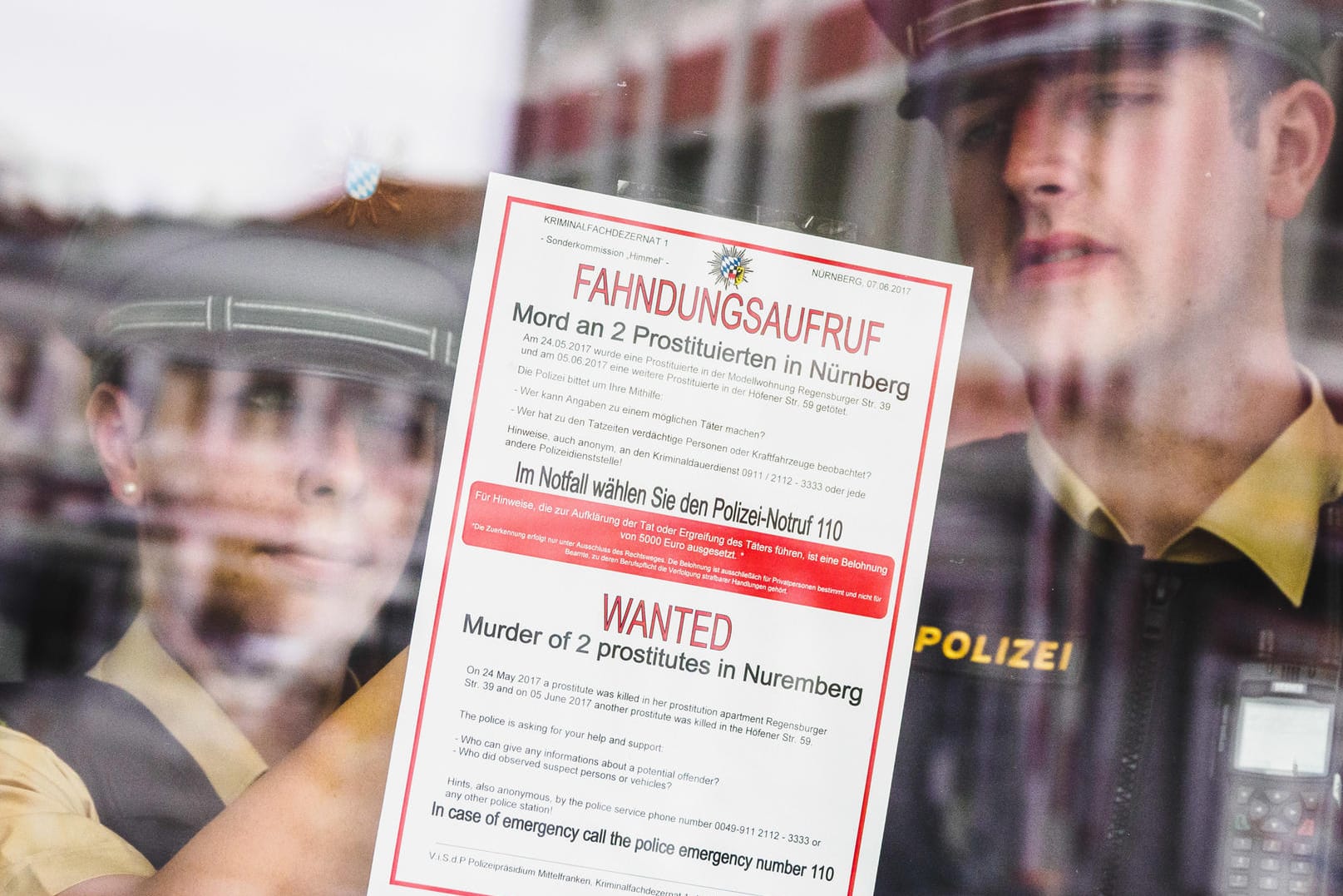 Polizisten kleben einen Fahndungsaufruf in verschiedenen Sprachen an eine Tür.