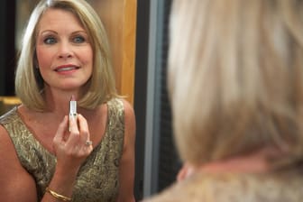 Eine reife Frau schminkt sich die Lippen vor einem Spiegel