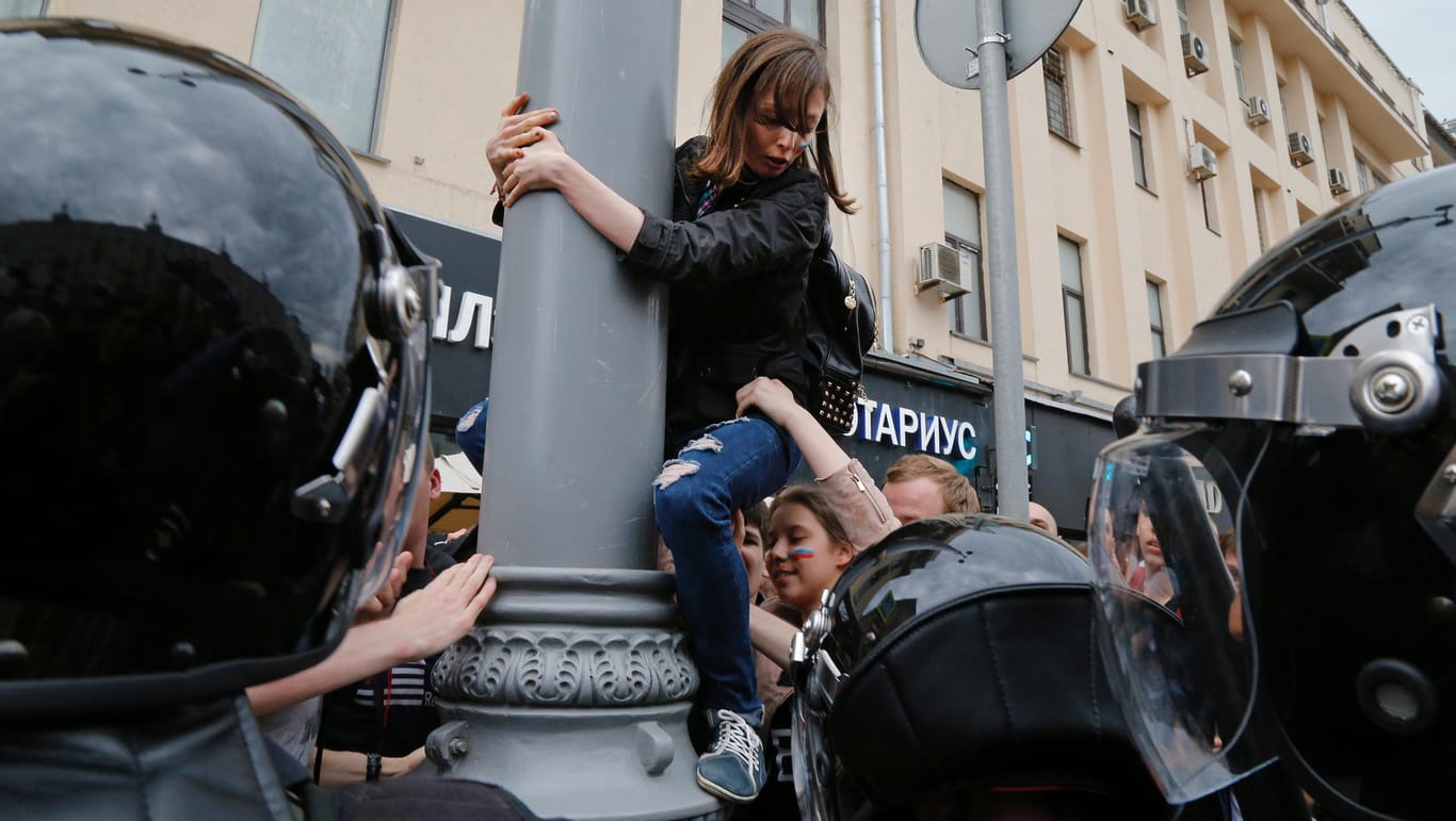 In Moskau wird eine Demonstrantin von einem Laternenpfahl gezerrt.