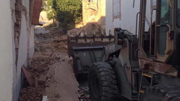 Ein Bulldozer räumte in einer Straße zwischen stark beschädigten Häusern Schutt weg.