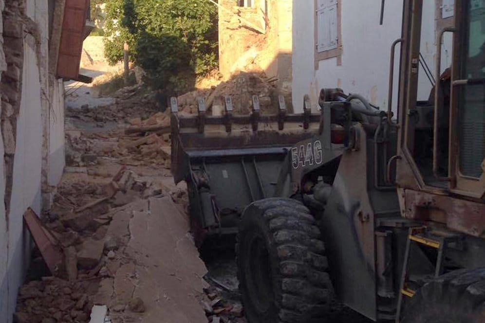 Ein Bulldozer räumte in einer Straße zwischen stark beschädigten Häusern Schutt weg.