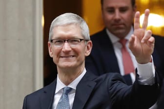 Apple-Chef Tim Cook macht in London das Victory-Zeichen. Apples Auto-Pläne musste er ändern