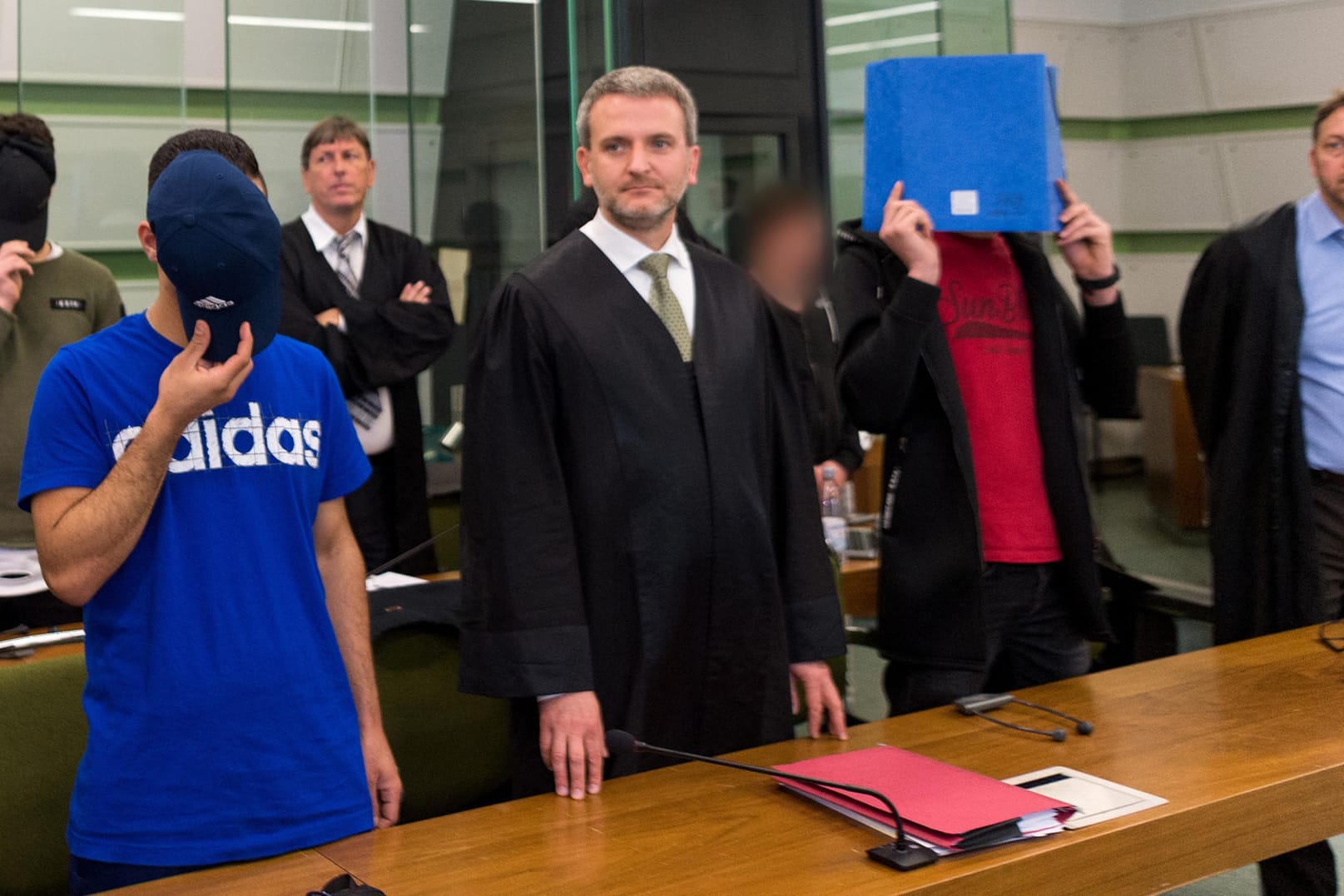 Vier der sechs Männer, die sich wegen gemeinschaftlichen versuchten Mordes verantworten müssen, stehen mit ihren Anwälten im Sitzungssaal des Berliner Landgerichtes.