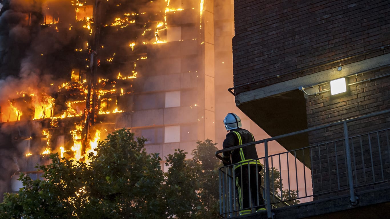 Ein Feuerwehrmann blickt von einem benachbarten Balkon auf das brennende Hochhaus.