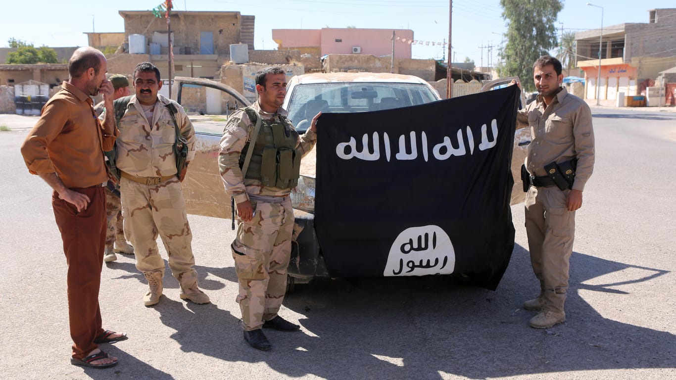 Kurdische Kämpfer halten im Irak eine eroberte IS-Flagge in die Höhe.