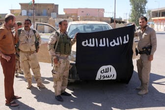 Kurdische Kämpfer halten im Irak eine eroberte IS-Flagge in die Höhe.
