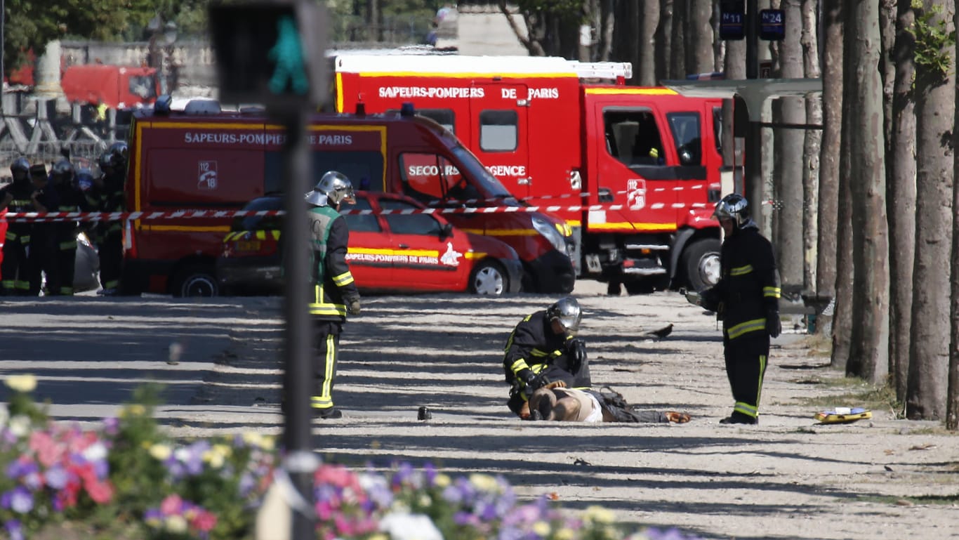Rettungskräfte untersuchen auf den Champs Elysees in Paris einen am Boden liegenden Mann . Ein Mann ist mit seinem Auto auf der Pariser Prachtstraße Champs-Elysées auf ein Fahrzeug der französischen Gendarmerie geprallt.