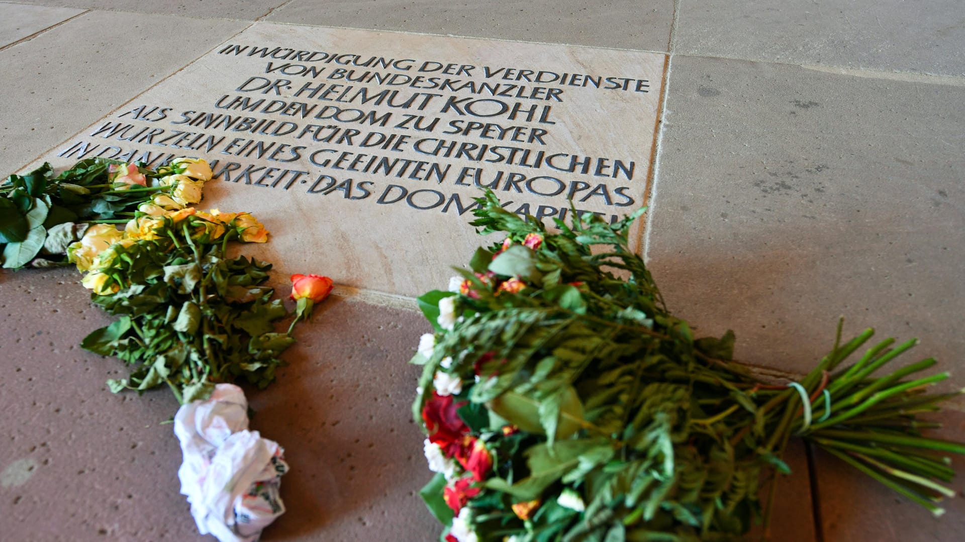 Neben einer Bodenplatte mit einer Danksagung an Helmut Kohl liegen in Speyer im Kaiserdom mehrere Blumensträuße.