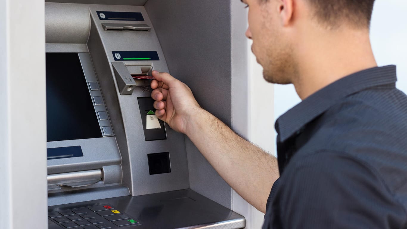 Junger Mann schiebt Bankkarte in den Geldautomaten