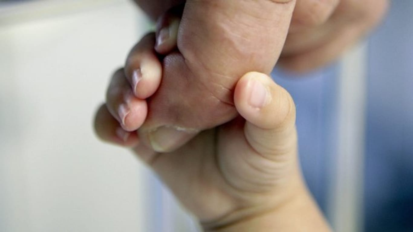 Die Hand eines Säuglings klammert sich an den Finger eines erwachsenen Mannes.