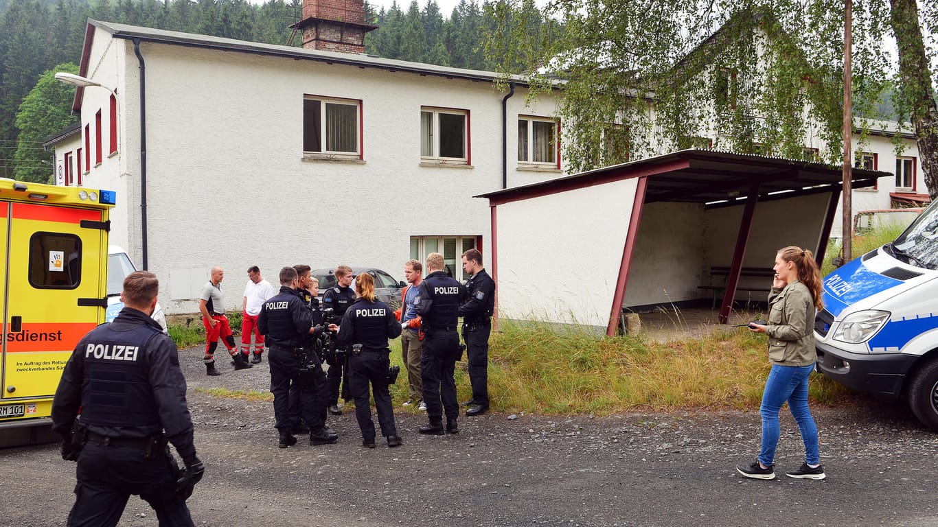 Polizisten und Sanitäter stehen vor einem der durchsuchten Gebäude in Haselbach (Thüringen).