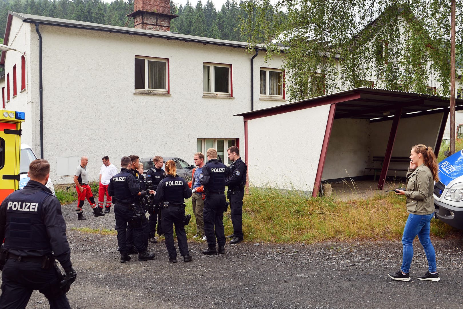 Polizisten und Sanitäter stehen vor einem der durchsuchten Gebäude in Haselbach (Thüringen).