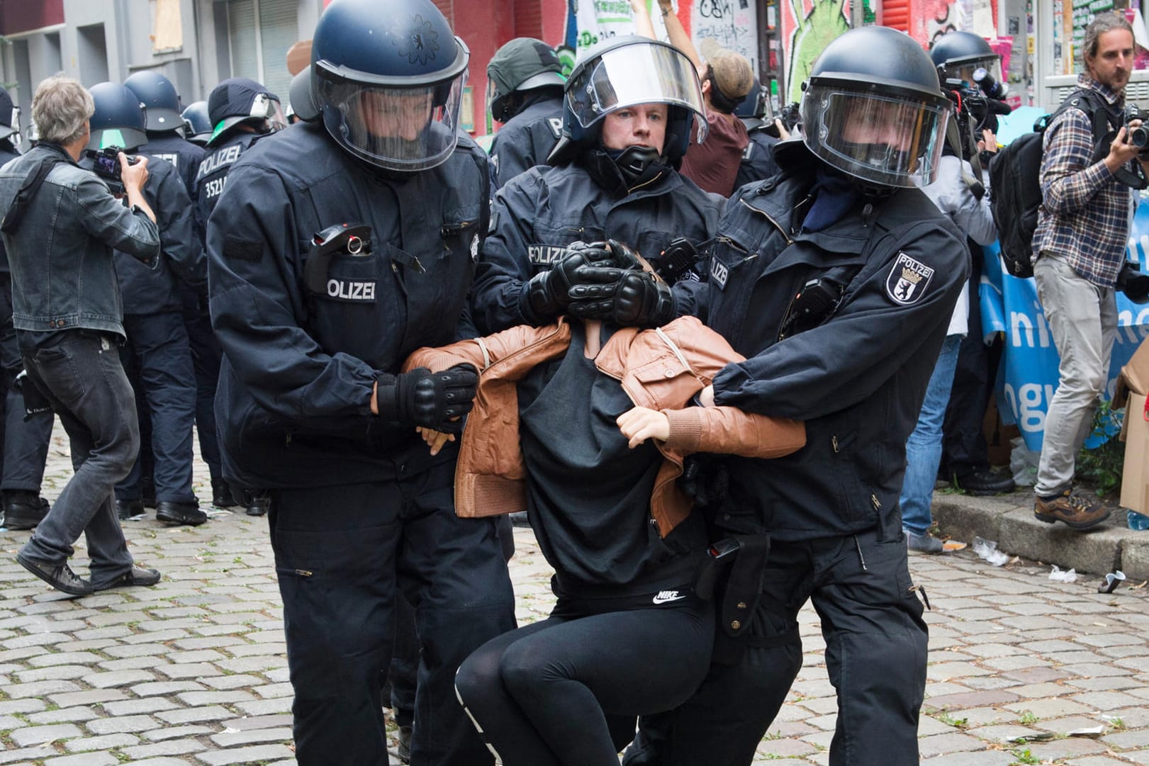 Polizisten tragen Demonstranten auf der Friedelstraße in Neukölln weg.
