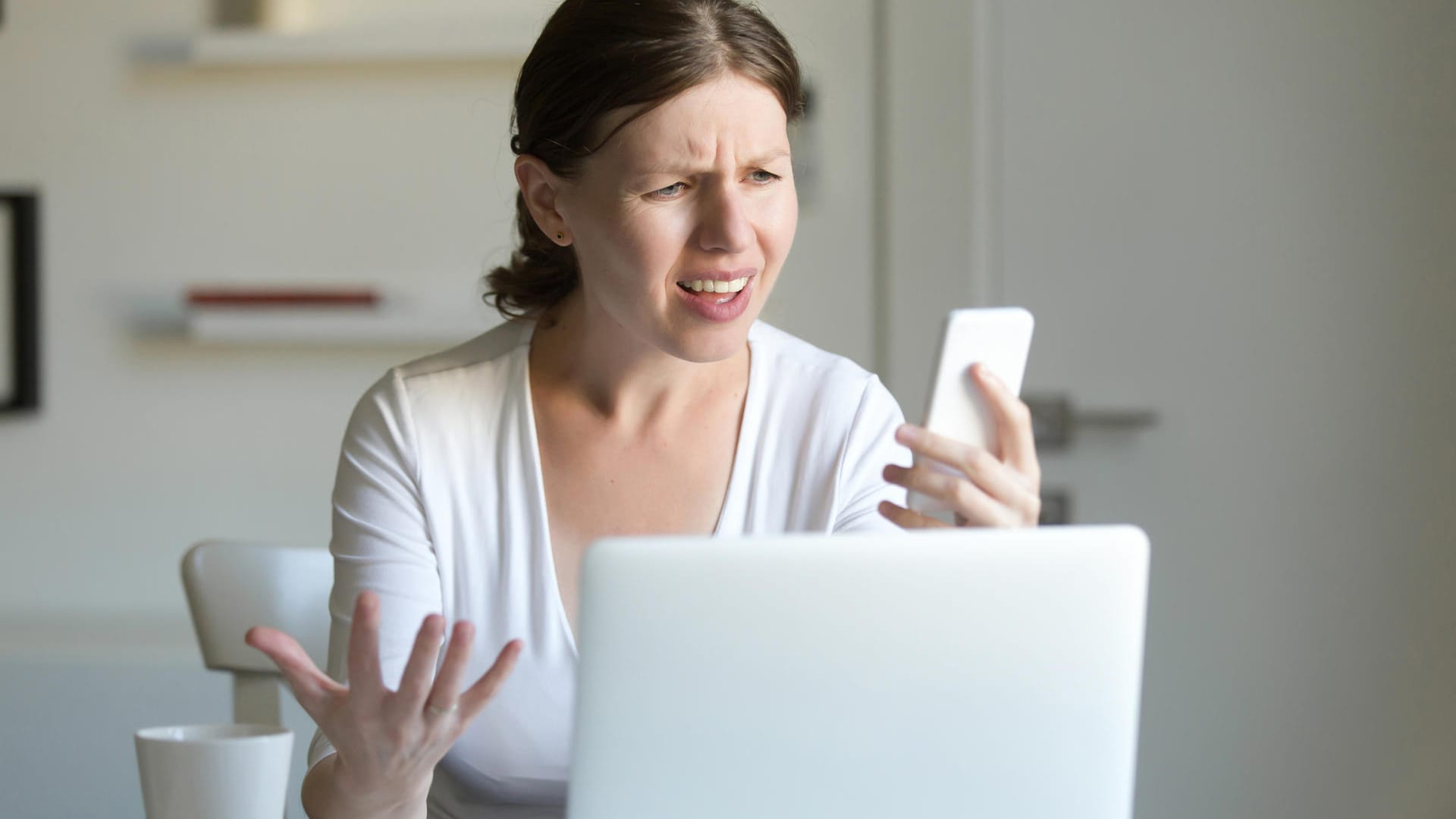 Eine Frau am Notebook schaut auf ihr Handy