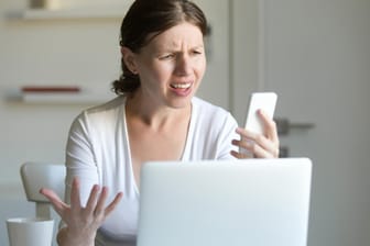 Eine Frau am Notebook schaut auf ihr Handy