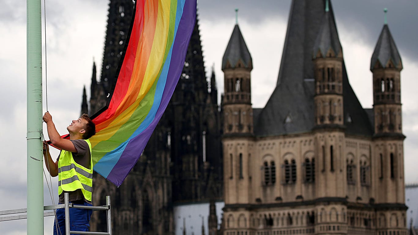 In Köln wird eine Regenbogenfahne gehisst, im Hintergrund der Dom Doms und die Kirche Groß St. Martin (re.).