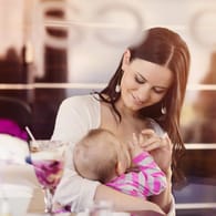 Eine junge Frau stillt ihre Tochter im Café: Manche Menschen sehen es zwiegespalten, wenn Mütter ihre Kinder in der Öffentlichkeit stillen.