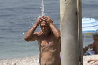 Ein Mann kühlt sich am Strand des Athener Vororts Alimos unter einer Dusche ab.