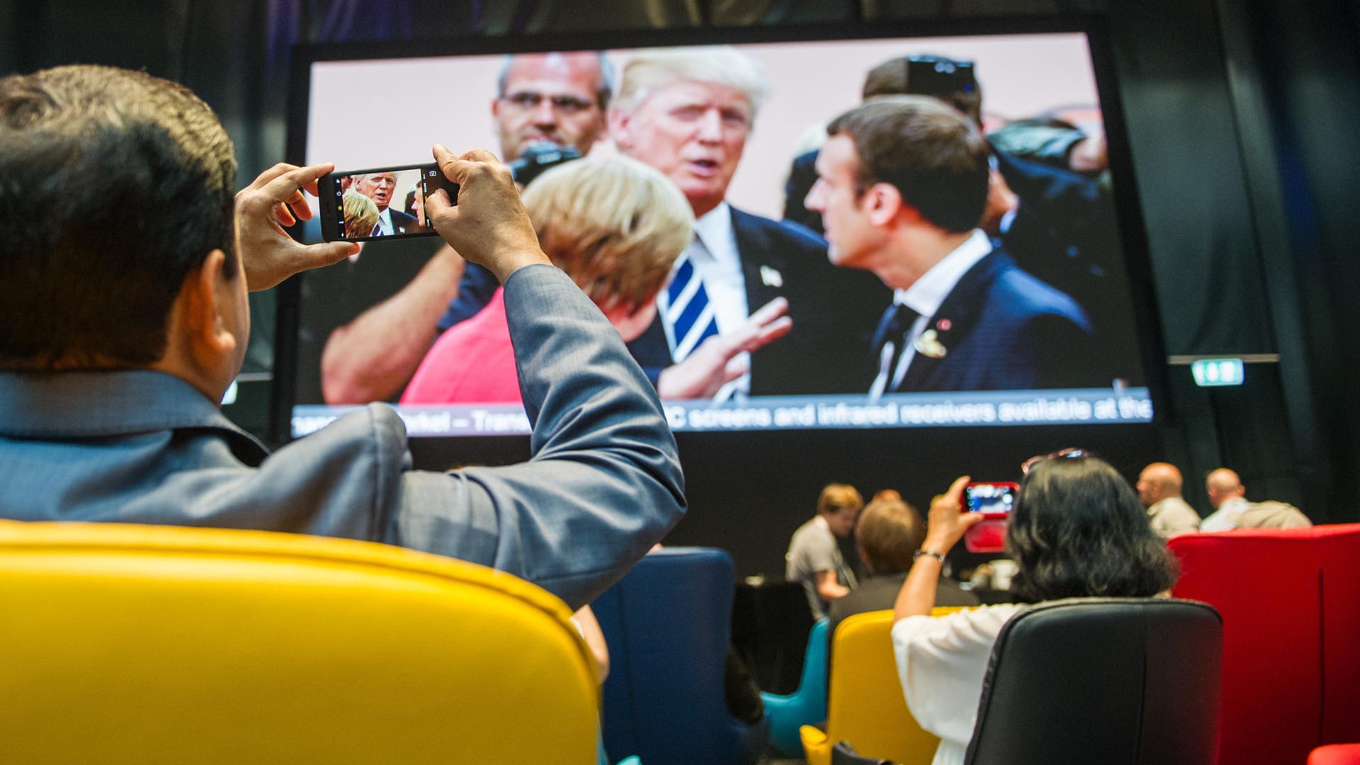 Journalisten machen im Medienzentrum für Journalisten, das anlässlich des G20-Gipfels eingerichtet wurde, ein Foto von dem Aufeinandertreffen von Bundeskanzlerin Angela Merkel, dem französischen Staatspräsidenten Emmanuel Macron und US-Präsident Donald Trump, die live auf einen Bildschirm übertragen wird.