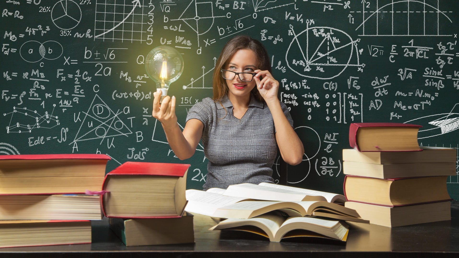 Frau vor einer Tafel mit Lampe in der Hand und einem Schreibtisch mit Büchern