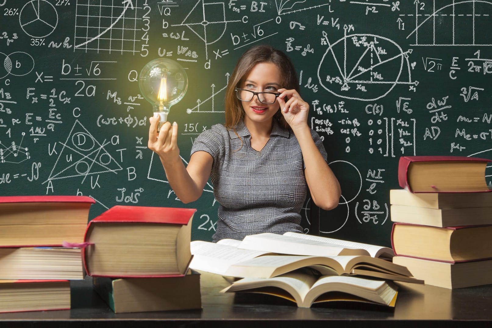 Frau vor einer Tafel mit Lampe in der Hand und einem Schreibtisch mit Büchern