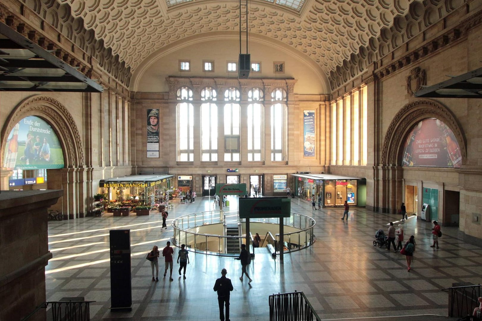 Fahrgäste und Passanten flanieren durch die Sonnenstrahlen durchflutete Westhalle des Leipziger Hauptbahnhofs.