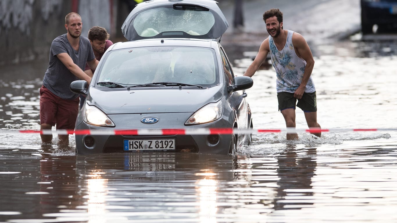 Männer schieben ein Auto aus dem Wasser einer überfluteten Straße in Köln.