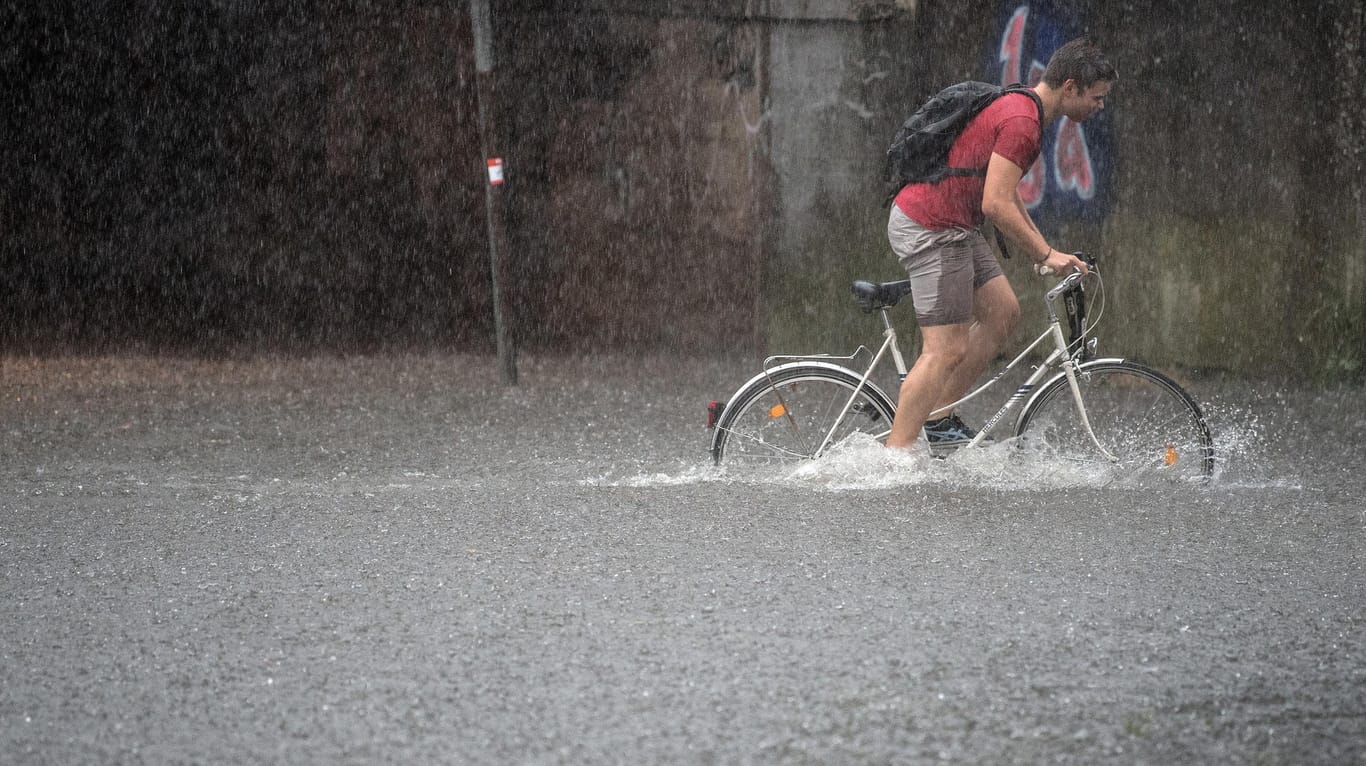 Ein Fahrradfahrer quält sich durch eine überflutete Straße in Köln.