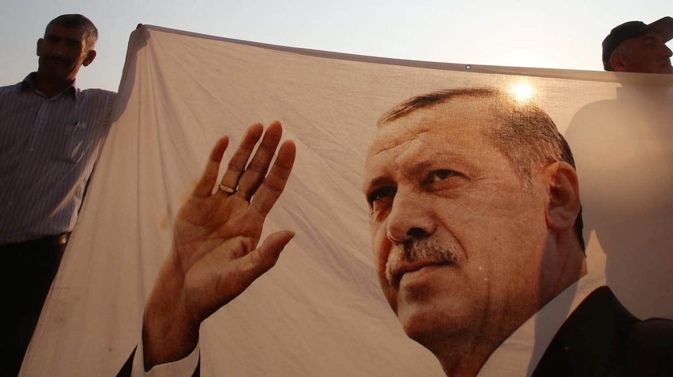 Männer halten bei der Eröffnung des Denkmals zum Gedenken an die Opfer des gescheiterten Putschversuchs ein Tuch mit dem Foto des türkischen Präsidenten Recep Tayyip Erdogan.