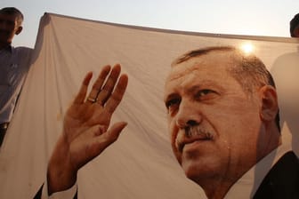 Männer halten bei der Eröffnung des Denkmals zum Gedenken an die Opfer des gescheiterten Putschversuchs ein Tuch mit dem Foto des türkischen Präsidenten Recep Tayyip Erdogan.
