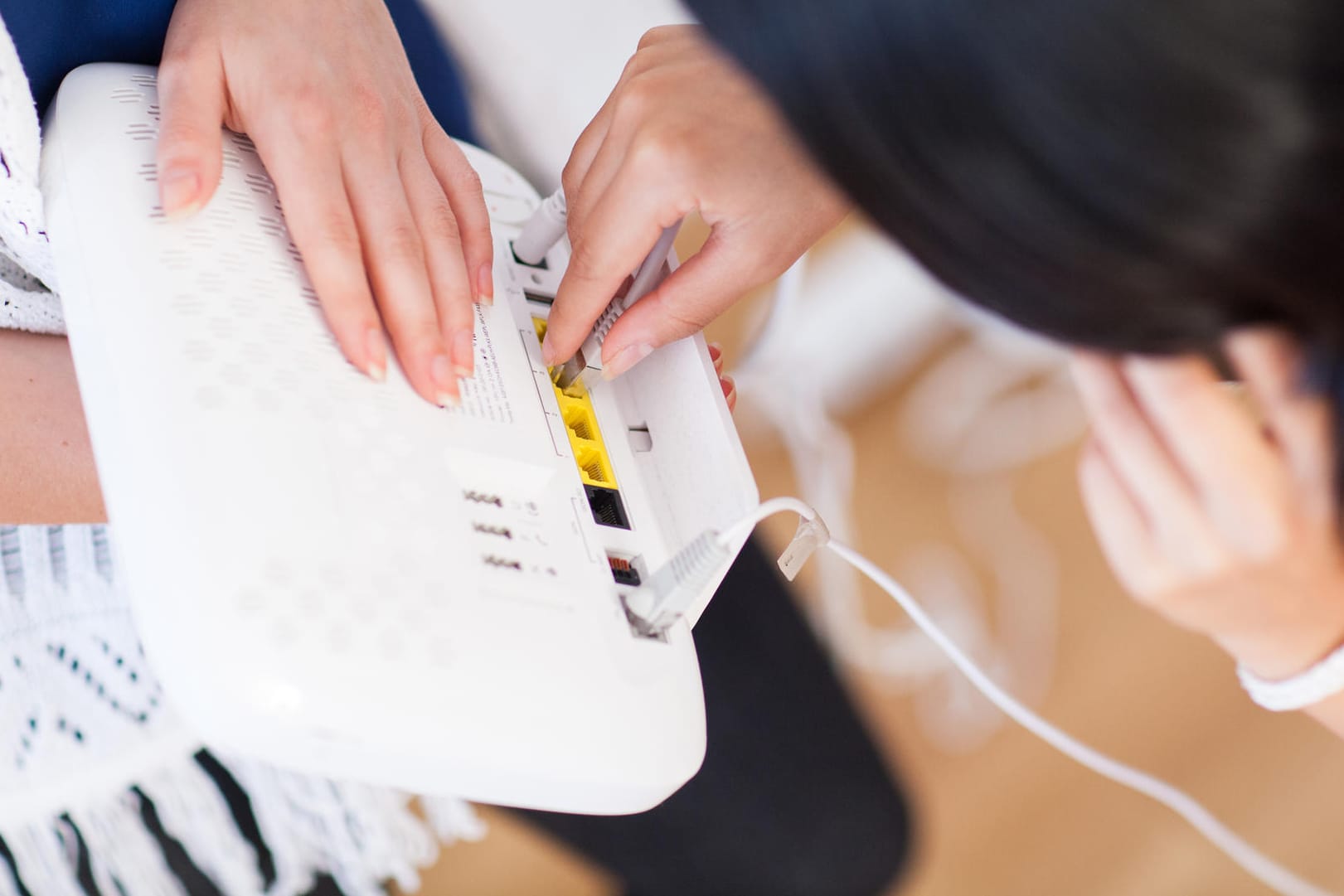 Eine Frau steckt ein Netzwerkkabel in den Router: Das BSI gibt Tipps, wie Verbraucher ihr Heimnetzwerk vor Hackerangriffen schützen können.