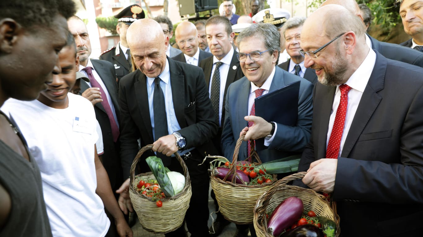 Martin Schulz, Enzo Bianco, Bürgermeister von Catania, und der italienische Innenminister Marco Minniti (li.) bekommen Körbe mit Gemüse aus dem Garten einer Flüchtlingseinrichtung in Catania geschenkt.