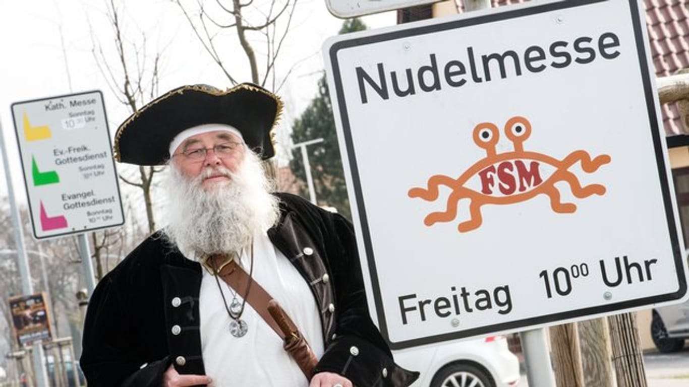 Rüdiger Weida vom Verein "Kirche der fliegenden Spaghettimonster" steht neben einem Schild, das für die "Nudelmesse" des Satirevereins im brandenburgischen Templin wirbt.