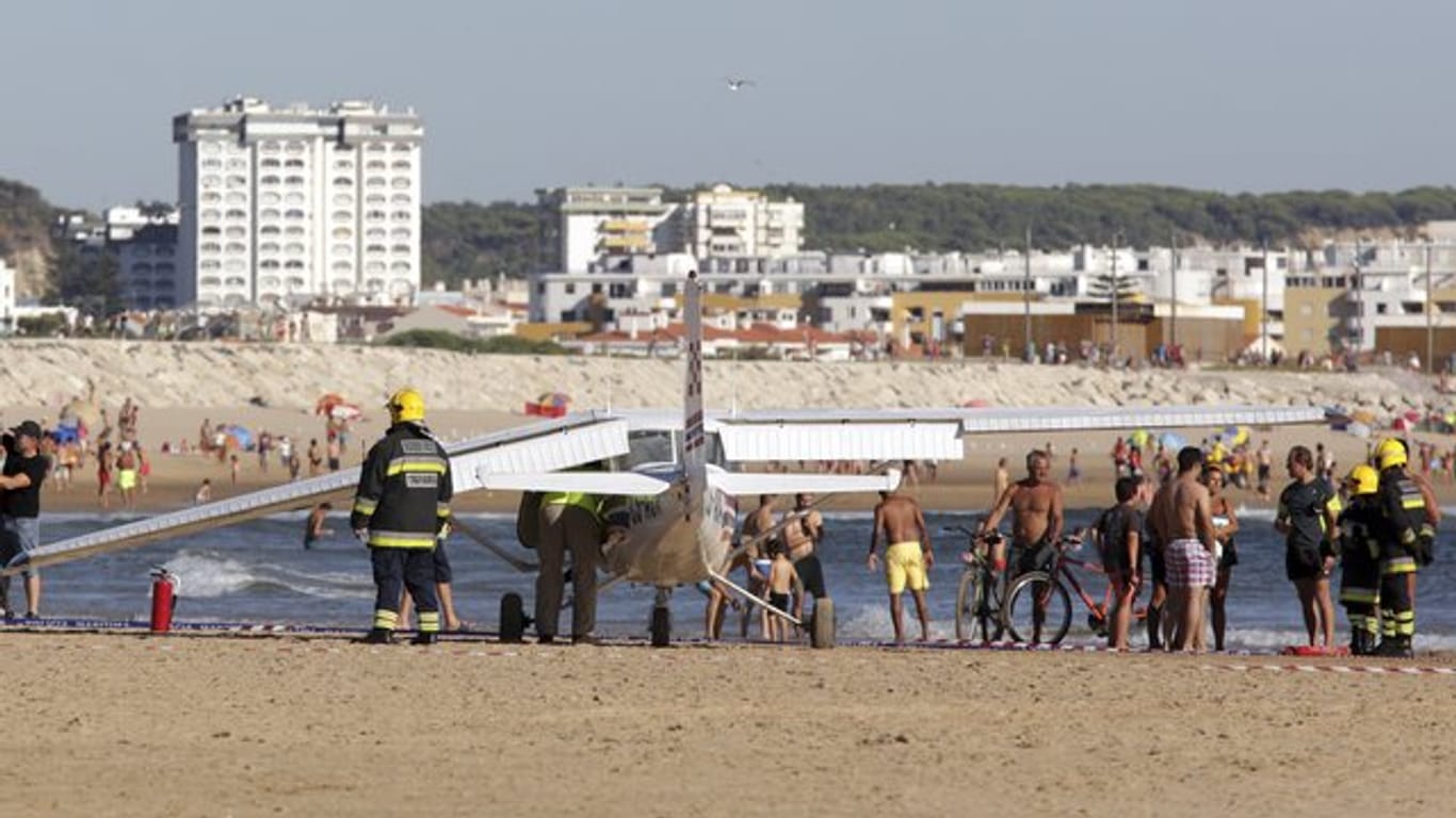 Feuerwehrleute stehen in Costa da Caparica, in der Nähe von Lissabon am Strand neben einem Kleinflugzeug, das am Sao Joao Strand notgelandet ist.