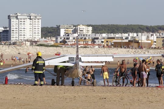 Feuerwehrleute stehen in Costa da Caparica, in der Nähe von Lissabon am Strand neben einem Kleinflugzeug, das am Sao Joao Strand notgelandet ist.