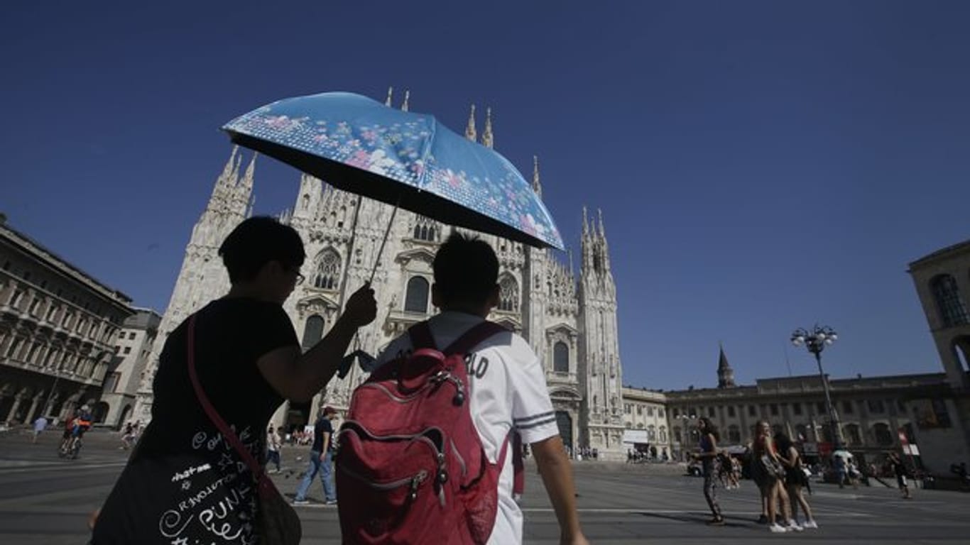 Touristen gehen in Mailand bei großer Hitze unter einem Sonnenschirm am Dom vorbei.