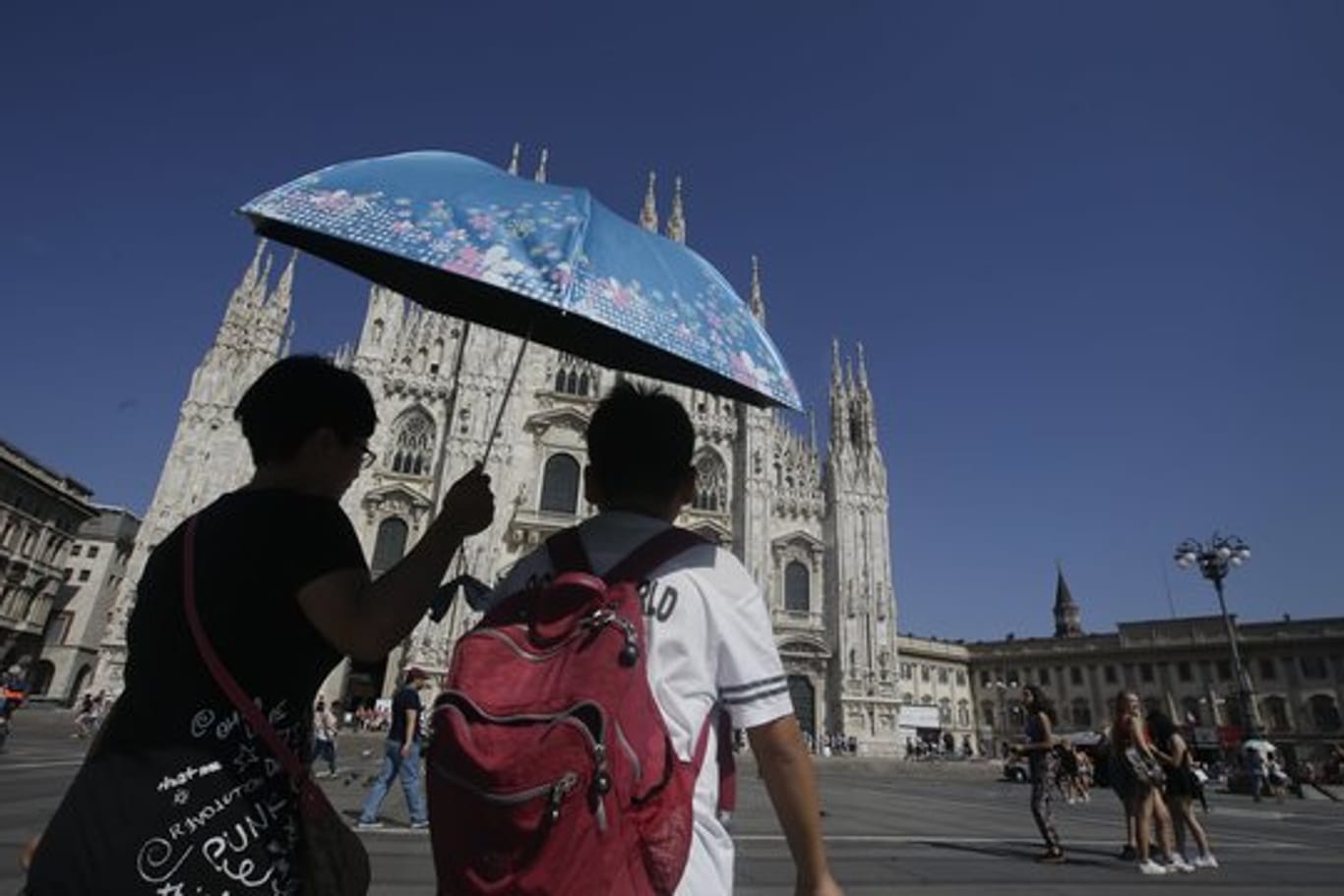 Touristen gehen in Mailand bei großer Hitze unter einem Sonnenschirm am Dom vorbei.